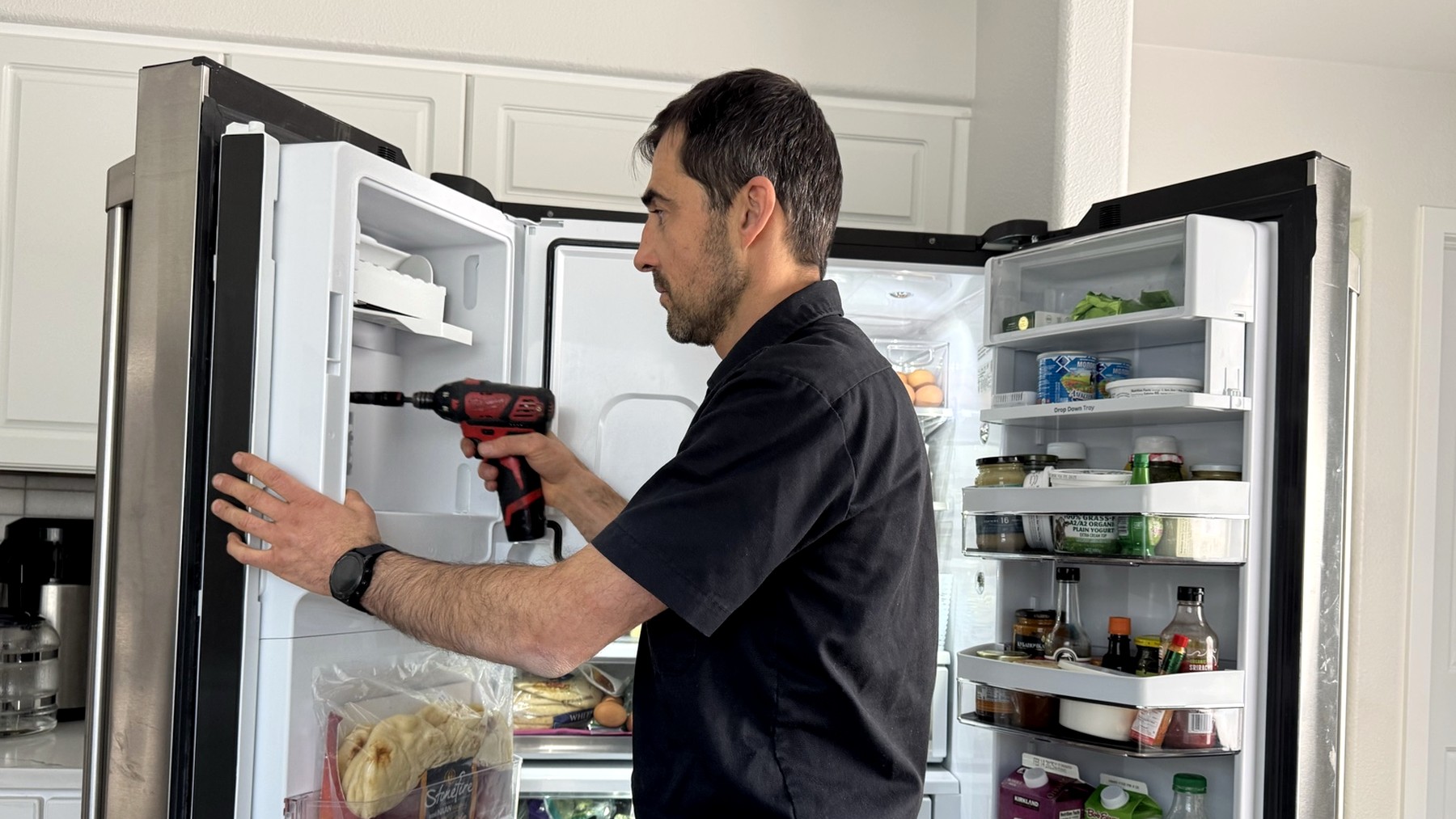 Technician repairing an ice maker inside an open refrigerator door